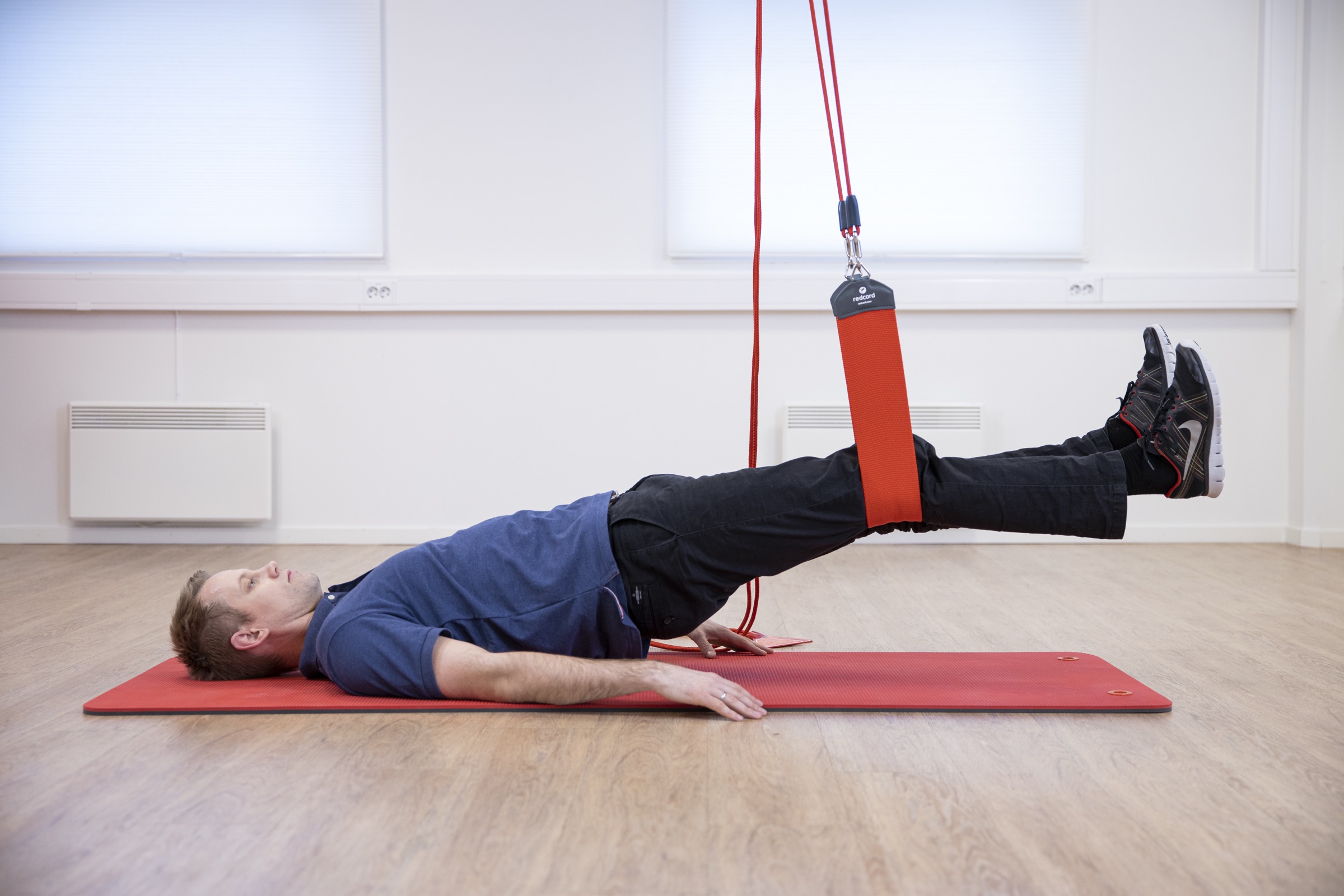 A person performing a supported bridge with legs held in Redcord slings